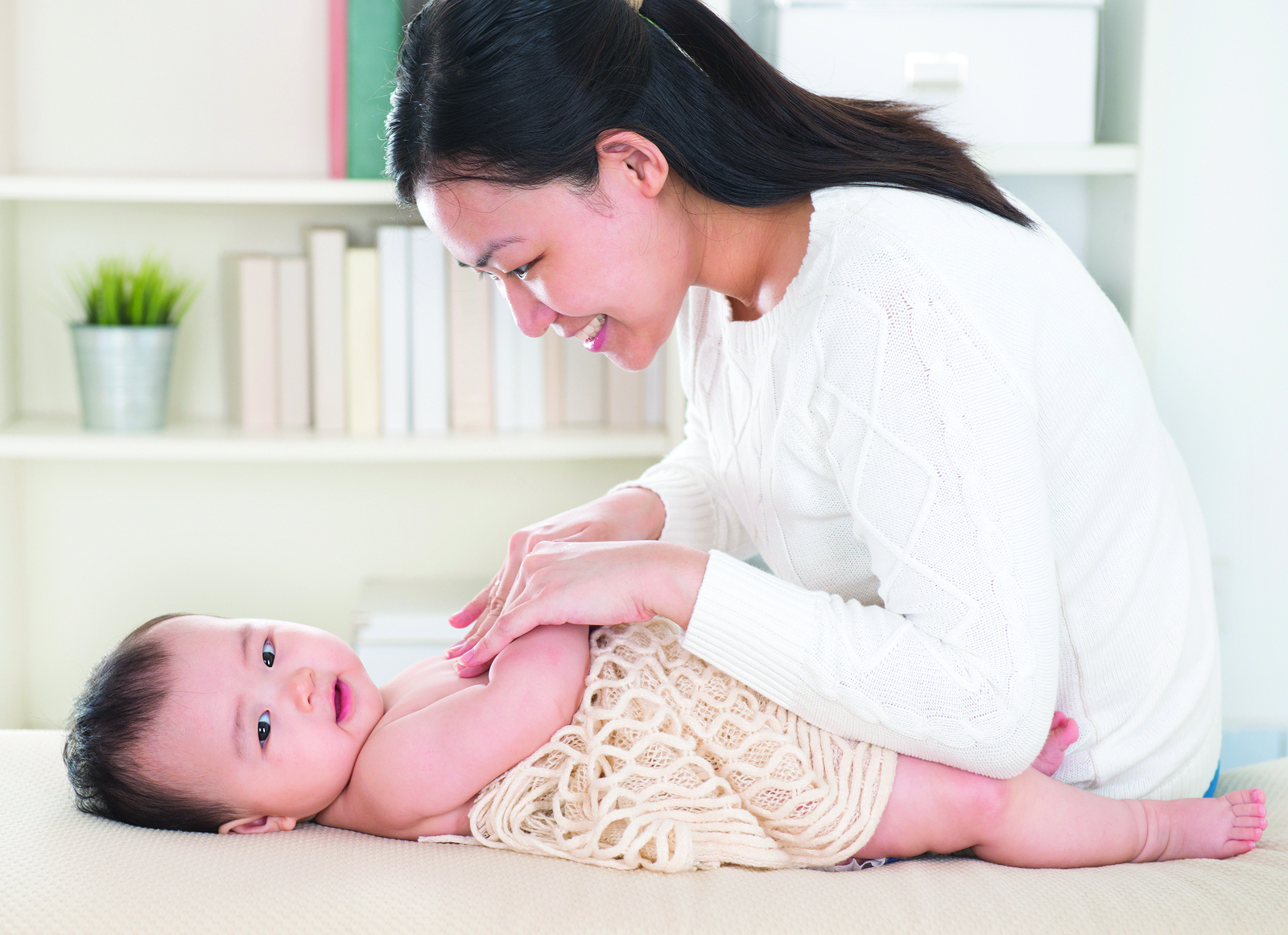 Asian mother giving massage to baby girl at home.