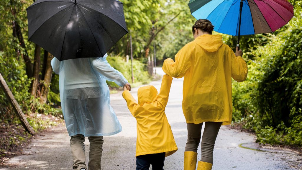 Family in rain gear, walking in the rain, using Human Nature DEET-free Skin Shield Oil for safe outdoor protection during the rainy season